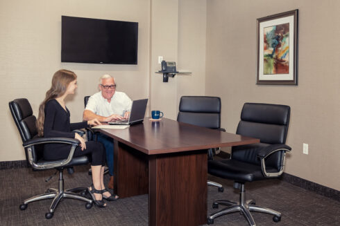 A young woman and an older man seated at a conference table, reviewing information on a laptop during a professional consultation.