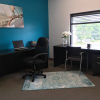 Office interior with a dark L-shaped desk, a teal accent wall, and nautical-themed decor.