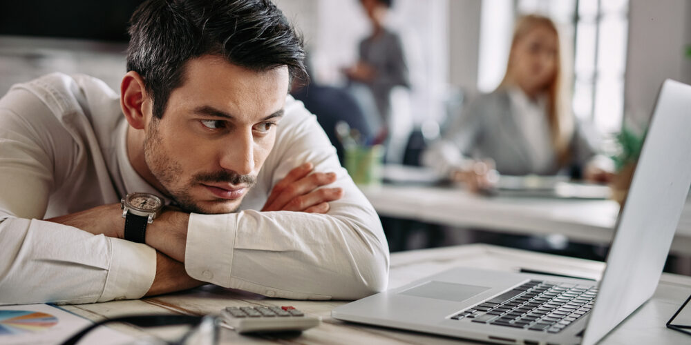 Young,Businessman,Leaning,On,His,Desk,And,Feeling,Bored,While