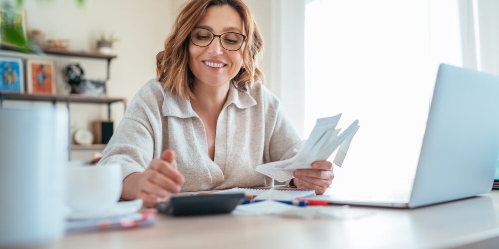 Beautiful,Middle-aged,Woman,In,Glasses,And,Paper,Bills,Joyfully,Laughing Startup founders discussing professional virtual business solutions in a modern virtual office setup with laptops and notebooks.