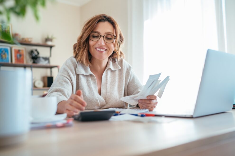 Beautiful,Middle-aged,Woman,In,Glasses,And,Paper,Bills,Joyfully,Laughing Startup founders discussing professional virtual business solutions in a modern virtual office setup with laptops and notebooks.